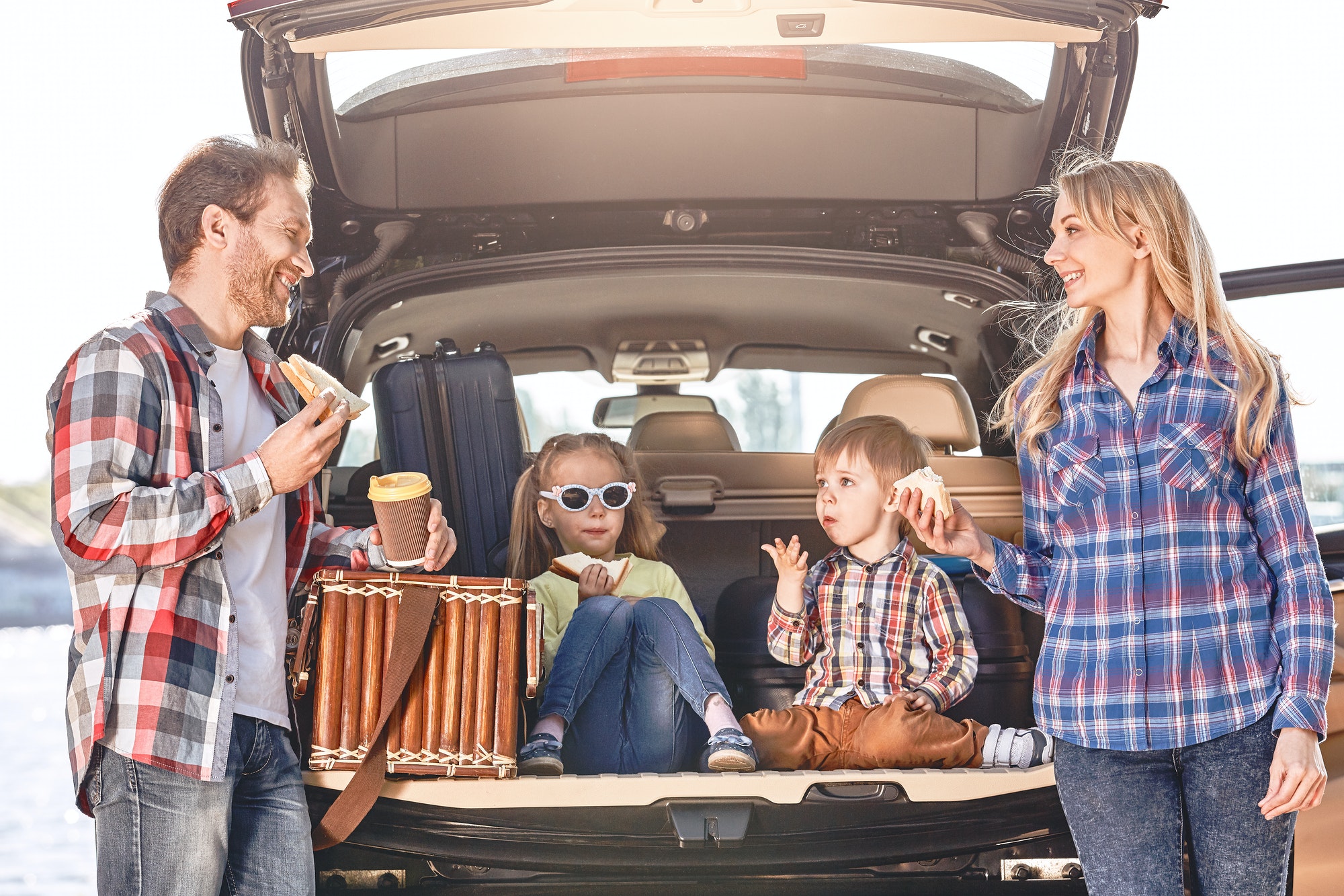 Snack time. Family stands near the car, having a lunch. Family road trip